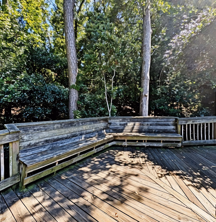 A weathered pressure-treated deck where shaded bench boards have gone grey and green while the open deck surface has bleached lighter